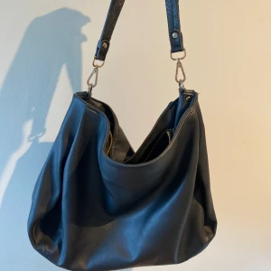 Svart väska - Hej! Säljer nu denna väska, jätte rymlig och bekväm. Får plats med dator och mer! Tyvärr lite slitningar på bandet men går att byta💕