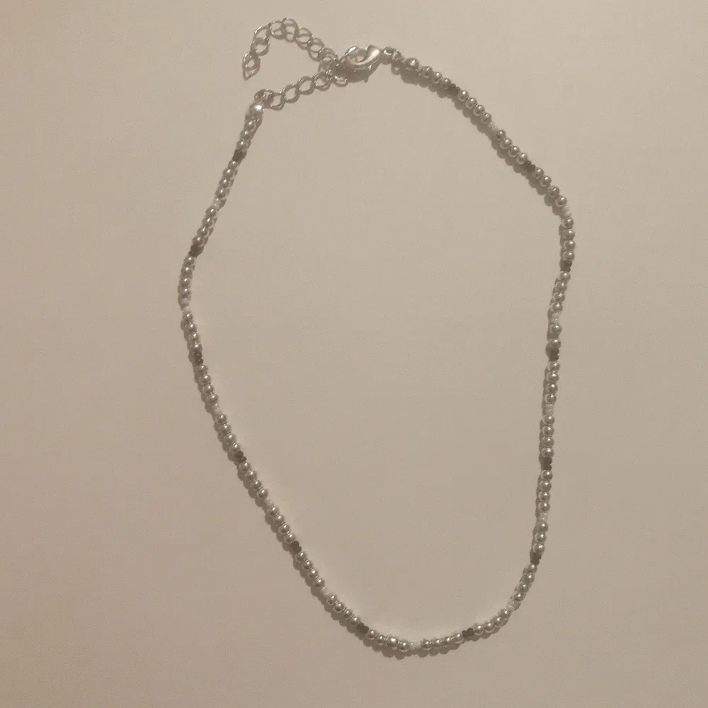 Halsband i silverfärg, inte äkta silver. Några svarta och vita pärlor med. Pärlorna är Små och halsbandet lite justerbart men stilen är att vara ganska litet runt halsen. . Accessoarer.