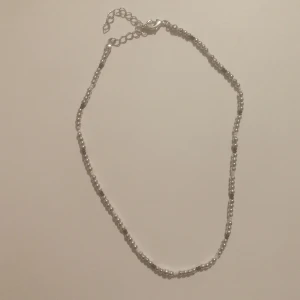 Pärlhalsband  - Halsband i silverfärg, inte äkta silver. Några svarta och vita pärlor med. Pärlorna är Små och halsbandet lite justerbart men stilen är att vara ganska litet runt halsen. 