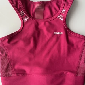 Rosa träningslinne, STRONGER, storlek XS - Superfint rosa träningslinne perfekt nu till sommaren!! Endast använd några gånger, i fint skick. På bilderna ser förgen ganska varm ut men skulle säga att det i verkligheten är en kallare rosa färg.  Lite reflex (bild 3)