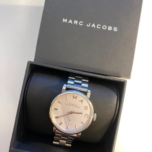 Marc Jacobs klocka - En stilren silvrig klocka från Marc Jacobs. Urtavlan har en diameter på 3,5cm. Nytt batteri sätts in innan leverans. Box, instruktionsbok och extra länkar medföljer. Klockan är använd så små naturliga repor finns på armbandet och glas. Inget som stör