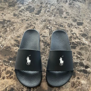 Polo Ralph Lauren Badsandaler - Ett par helt oanvända (endast testade) svarta badsandaler från det välkända och lyxiga varumärket Ralph Lauren. Digitalt kvitto finns som autentisering.