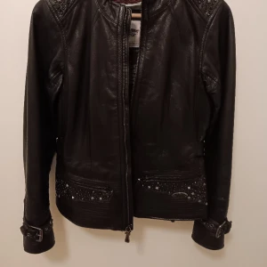 Skinnjacka fodrad - En klassisk bikerjacka för Dam. Strl Small, svensk 38. Kraftigt figursydd med nitar och swarowski-kristaller. Midja och ärmslut kan varieras med spännen.Inköpt i Florida.