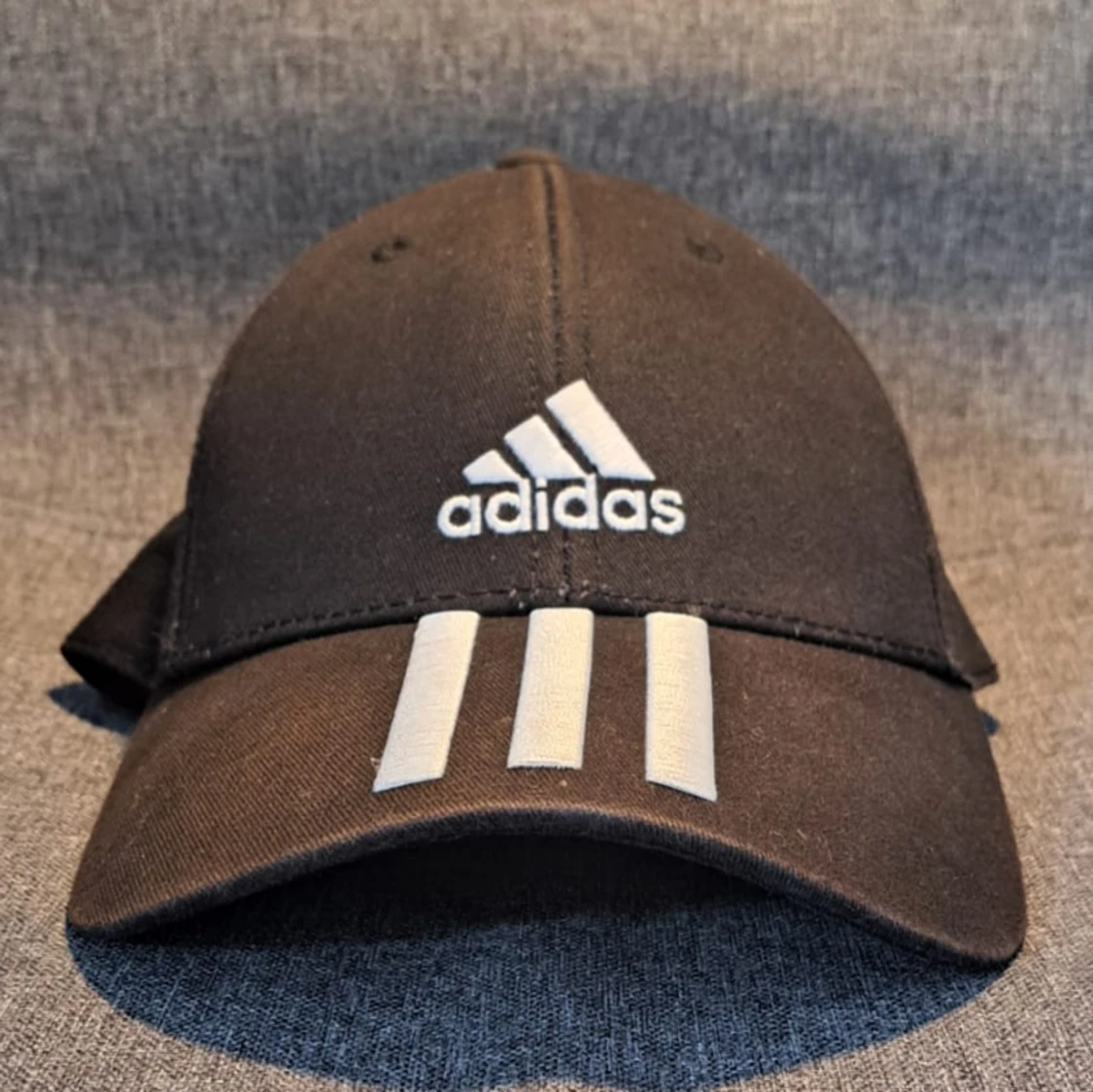 En svart adidas keps med vitt adidas märke och ränder.