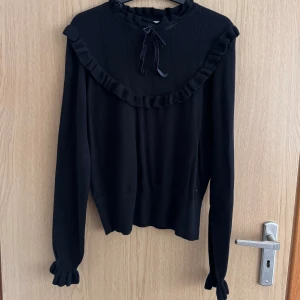 Broderad tröja  - En svart broderad tröja med en rosett i mjukt tyg. Rik på detaljer i både ärmar och på bröstet. 