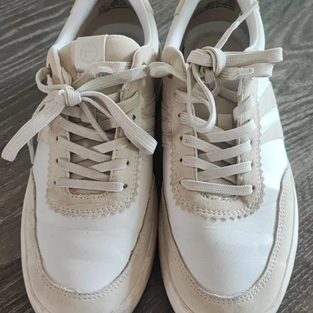 Ett par vita sneakers från Tamaris med snörning och detaljer i beige. Skorna har en klassisk design med en bekväm sula.. Skor.