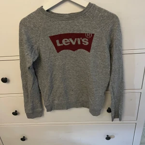 Grå tröja från Levi's - En grå långärmad tröja från Levi's med röd logotyp på bröstet. Tröjan har en rund halsringning och är tillverkad i ett mjukt material. helt okej skick! 