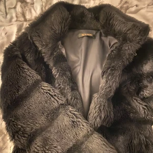 Fluffig jacka - Superfin svart (fejk) päls jacka. Har tyvärr ett hål på armen (se bild 5) men man tänker inte på de då det sitter på insidan och det inte syns när man har på sig jackan. Lätt att sy igen❣️