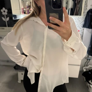Vit blus - En elegant vit blus med långa ärmar och knappar framtill. Blusen har en klassisk krage och är tillverkad i ett lätt och luftigt material, vilket gör den perfekt för både vardag och fest. fläck på ryggen som knappt syns och lite smink fläckar i kragen.någon liten tråd lös inget som märks heller köpt second hand