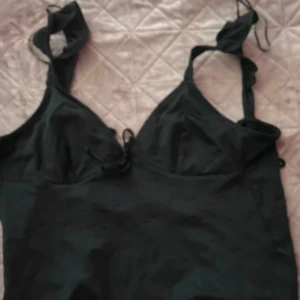 Svart bikini - Ett svart linne med knytband och volangdetaljer. Linnet  har en öppen rygg och ett av banden har gått sönder men går enkelt att sy in då de bara är en sida den lossnat från.