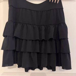 Svart volangkjol - En svart kjol med flera lager av volanger. Kjolen har en normal passform och är kort i längden.