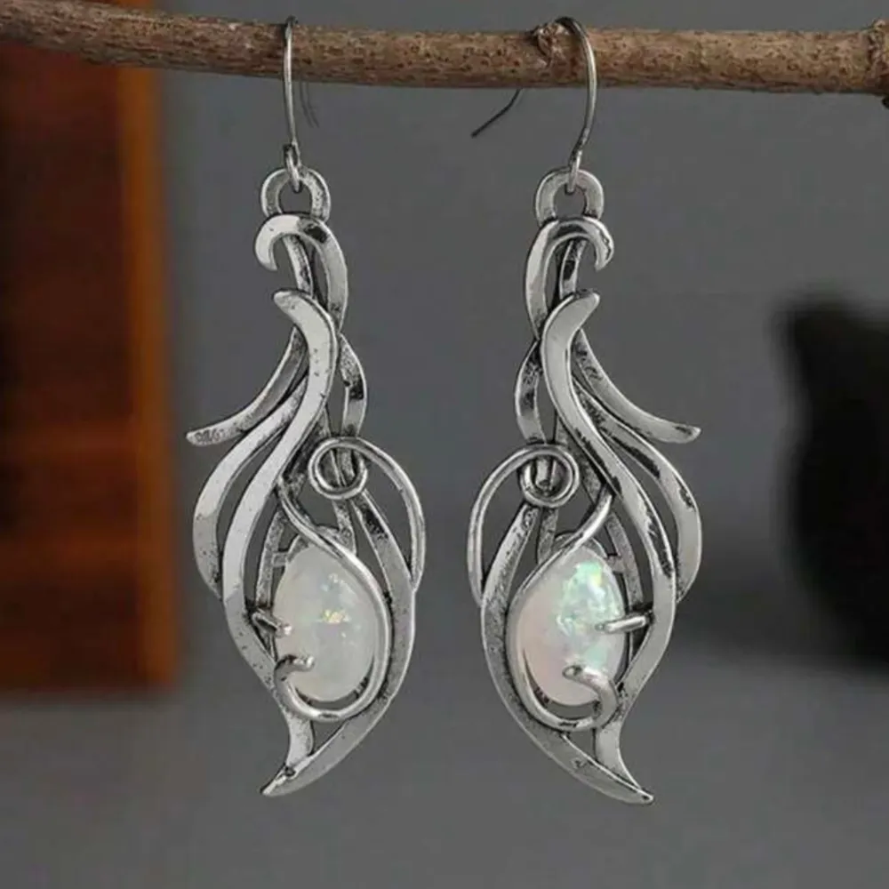 Ett par nya eleganta örhängen i vintagestil. De är silverfärgade med en unik, böljande design. Örhängena har infällda vita stenar som ger en gnistrande effekt. Opallikande konststenar. 5,5 cm långa, 1,8 cm breda. Krokar. Perfekta för både vardag och fest. Jag ger bundlerabatt.. Asusteet.