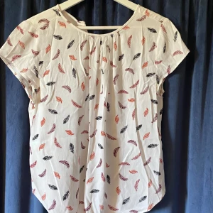 Blus - En vit blus med fjädrar i olika färger
