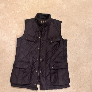 Barbour vest  - Säljer nu denna vest som Inte är använd på jätte länge. Säljer billigt då jag bara vill bli av med den. Kom gärna med pris förslag. Den är väldigt mörk blå, ser nästan svart ut 