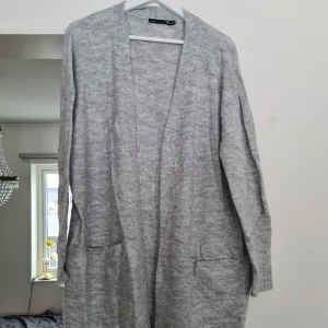 Grå lång kofta  - Ljusgrå lång kofta med kofta. Aldrig använd, nyskick, normal i storleken (XS/S). Kom med prisförslag   Material: 71% Akryl, 26% Polyester, 3% Elastan. 