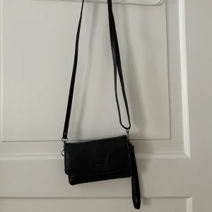 Skinnväska Casal - Liten svart axelremsväska i skinn från Casal. Använd en gång, som ny. Flera fack inuti. Går ett reglera bandet. Bredd: 11,5cm. Längd: 17cm. Bara att fråga om det är något du undrar! Kan mötas på Järntorget i Göteborg eller skicka. Finns fler bilder. 