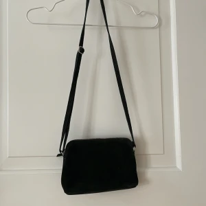 Mörkgrön väska i mocka - Liten mörkgrön axelremsväska i mocka. Använd en gång, som ny. Ett litet fack på insidan och ett på utsidan. Stängs med dragkedja. Går att reglera bandet. Bredd: 14cm. Längd: 23cm. Bara att fråga om det är något du undrar! 