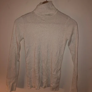 Vit polotröja - Bra skick. Stretchigt tyg, formar sig efter kroppen. Långärmad. Kragen går att vika ut och vika som man vill. 70% viskos och 30% polyamid. Stickad med tunn tråd.   Mer exakta mått kan ges på förfrågan. 