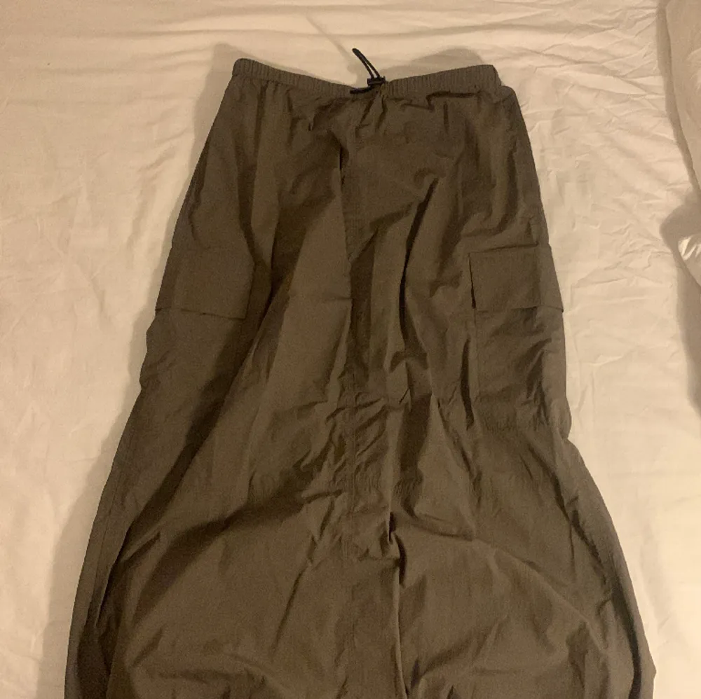 En lång kjol som är i ett tyg som liknar parachute byxor. En grön grå färg. Helt ny. Inga hål och oanvänd. Kjolar.