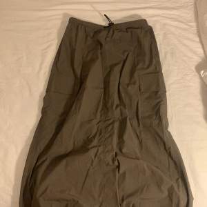 En lång kjol som är i ett tyg som liknar parachute byxor. En grön grå färg. Helt ny. Inga hål och oanvänd