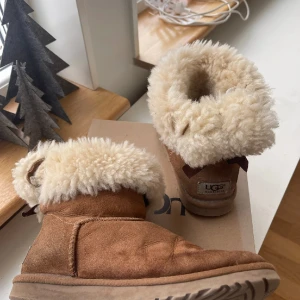 Beiga Uggs - Säljer mina beiga Uggs med rosetter på baksidan. Skorna går att vika ner. Uggsen har missfärgningar och slitage (kolla bilderna) lägre pris vid snabb affär🤍
