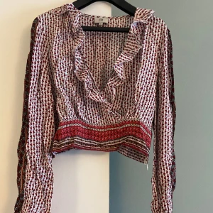 Blommig topp - Blommig topp med djup v-ringning, långa ärmar och kort i midjan. Storlek 38. Köpt på River Island. 