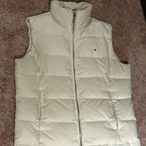 Använd, fast fin vit dunväst  - Tommy Hilfiger tunnare dunväst med några år på nacken.  Fräsch och fin ändå. Rak modell för dam fast kanske kan gå även för kille, smaksak ;)