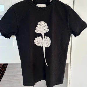 Our Legacy AW15 Big Acorn Tee, size 44 - Unik t-shirt med broderad blomma på sig från Our Legacy. Väldigt gott skick, köptes på secondhand för nåt år sen. Size 44 fits XS/S då ärmarna har släppt fåll. Kan mötas i Sthlm!