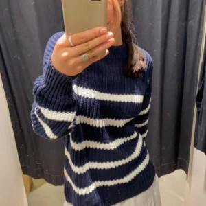 Mörkblå och vit randig stickad tröja - Säljer en supermysig mörkblå och vit randig stickad tröja. Den har en normal passform och är långärmad, perfekt för höst och vinter. Tröjan är i bra skick och väldigt bekväm att ha på sig. Perfekt för att hålla sig varm och snygg under de kallare månaderna!