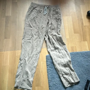 Beige linnebyxor med snörning - Säljer ett par bekväma beige linnebyxor med snörning i midjan. Byxorna är perfekta för en avslappnad look och är gjorda av ett lätt och luftigt material. De har en liten reva på ena benet, men det påverkar inte användningen. Perfekta för sommaren! 🌞