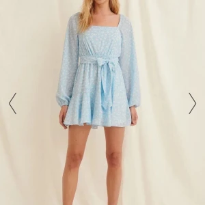 Ljusblå blommig klänning med knytband - Säljer en superfin ljusblå klänning med blommigt mönster. Den har långa ärmar och ett knytband i midjan som ger en fin passform. Klänningen är perfekt för sommar och vår, och passar både till fest och vardag. Den är i nyskick och har en söt volangdetalj längst ner.