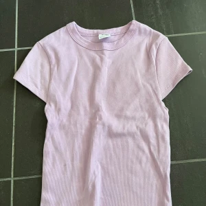 Ljuslila ribbad t-shirt från Bershka - Säljer en söt ljuslila t-shirt från Bershka i storlek XS. Den är ribbad och har korta ärmar, perfekt för sommaren! T-shirten är i bra skick och superbekväm att ha på sig. Passar både till vardags och fest. 🌸