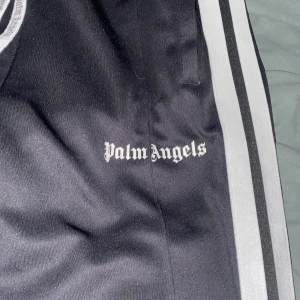 Svarta mjukisbyxor från Palm Angels - Säljer ett par svarta mjukisbyxor från Palm Angels. Byxorna har vita ränder längs sidorna . De är i bra skick och väldigt bekväma. Perfekta för en avslappnad stil eller träning. 