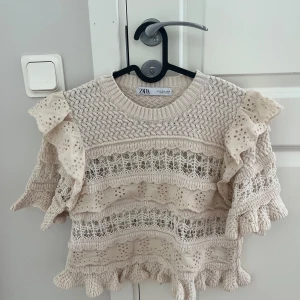 Beige stickad topp från Zara - Säljer en söt beige stickad topp från Zara. Superfint spetsmönster och volanger, den har använts någon enstaka gång😊 Skriv om du har funderingar eller något annat💕