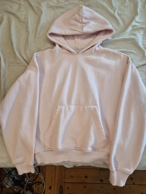 Ljusrosa hoodie med magficka - En ljusrosa hoodie med klassisk huva och stor magficka framtill. Hoodien har ribbade muddar vid ärmslut och nederkant. Perfekt för en chill och avslappnad stil. Tillverkad i mjukt material som känns skönt mot huden.