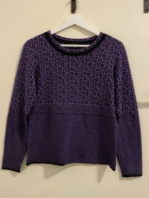 Lila mönstrad stickad tröja - Säljer en lila stickad tröja från Clay Knit med coolt leopardmönster upptill och grafiskt mönster nedtill. Tröjan har rund halsringning med svart kant och långa ärmar. Perfekt för dig som vill sticka ut med färg och mönster. Mått: längden är ca 59cm, axelbredden är ca 41cm och ärmlängden är ca 57cm 💕
