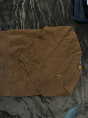 Brun sweater från Polo Ralph Lauren - Säljer en brun sweatshirt från Polo Ralph Lauren med rund halsringning och diskret logobrodyr på bröstet. Tröjan är långärmad och är gjord i mjukt bomullsmaterial. Perfekt för en avslappnad och stilren look. (Äkta) 