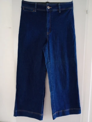 Mörkblå raka jeans med hög midja - Säljer ett par mörkblå jeans med rak passform och hög midja. Jeansen har klassisk femficksdesign, bälteshällor och knappgylf. Materialet är kraftig denim i bomull. Perfekta för en avslappnad och trendig look.
