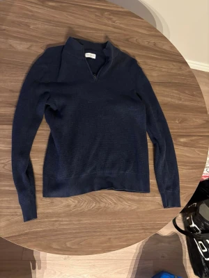 Mörkblå stickad tröja med halv dragkedja köpt på Volt - Mörkblå stickad tröja med lång ärm och halv dragkedja vid halsen. Tröjan har en enkel, stilren design och är tillverkad i ett mjukt stickat material. Perfekt för lager på lager och passar till det mesta.