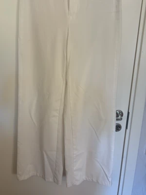 Vida vita linnebyxor - Säljer ett par snygga, vida kostymbyxor i vitt. Byxorna har hög midja och raka ben för en avslappnad och trendig look. Perfekta till sommaren och lätta att matcha med olika toppar. Materialet känns luftigt och skönt.