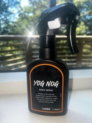 Yog Nog Body Spray från Lush - Yog Nog Body Spray från Lush i en svart plastflaska med spraymunstycke. Doften har toner av kola, kryddnejlika och ylang ylang. Flaskan rymmer 200 ml och har en modern, ungdomlig design med vit text och orange kantlinje. Har sprayat 4 gånger