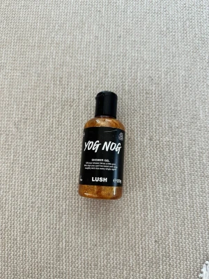 Lush Yog Nog duschgelé 120g - Lush Yog Nog duschgelé i en 120g flaska. Gelen är gyllene med skimrande glitter och har en krämig konsistens. Flaskan är svart med vit text och har en praktisk flipkork. Perfekt för dig som vill ha en lyxig duschupplevelse. Oöppnad och oanvänd 