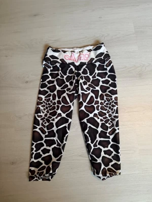 Gavelo leggings med giraffmönster - Snygga leggings från Gavelo med unikt giraffmönster i brunt, svart och vitt. Hög midja med bred resår och logga framtill. Stretchigt material som sitter skönt och formar sig efter kroppen. Perfekta för träning eller chill.