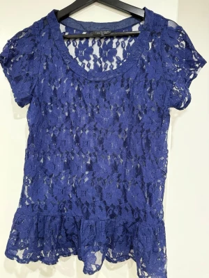 Blå spetsblus med volangkantTopshop - Snygg blå blus i spets med korta ärmar och volangkant nedtill. Blusen är genombruten och har rund halsringning. Perfekt för dig som vill sticka ut med en feminin och trendig topp.