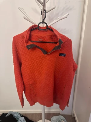 Röd quiltad tröja från L.L.Bean - Säljer en röd quiltad stickad tröja från L.L.Bean med tryckknappar vid kragen och fickor på sidorna. Tröjan har ett rutmönster och en liten logga på bröstet. Perfekt för dig som gillar en avslappnad men snygg stil.