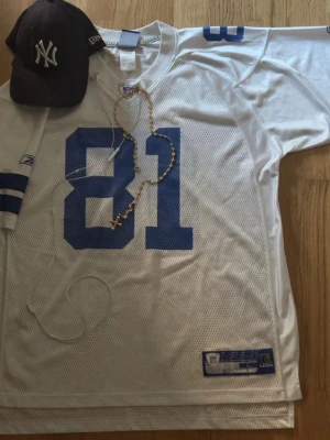NFL streetwear jersey - Säljer en vit NFL tröja med blått nummer 81 på framsidan. Tröjan har meshmaterial för extra ventilation och blå detaljer på ärmarna. Perfekt för sommar och passar perfekt in med streetwear stilen 