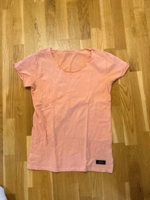 Ljusrosa Adrian Hammond t-shirt medium - En enkel och stilren ljusrosa t-shirt med rund hals och korta ärmar. Tillverkad i mjuk bomull, perfekt för en avslappnad look. Liten diskret etikett nertill på framsidan. Adrian Hammond medium