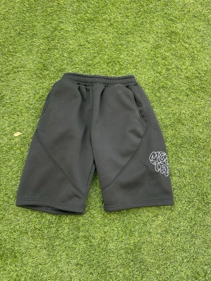 Mertra shorts  - Säljer ett par svarta shorts med coolt vitt tryck på ena benet. Shortsen har elastisk midja och två fickor framtill. Perfekta för sommaren och riktigt sköna att bära till vardags eller träning.