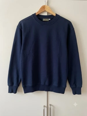 Mörkblå basic sweatshirt - En enkel och stilren mörkblå sweatshirt med rund halsringning och ribbade muddar vid ärmslut och nederkant. Perfekt för en avslappnad look och lätt att matcha med andra plagg. Tillverkad i mjukt material för extra komfort.