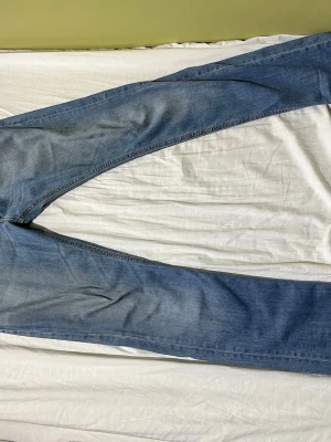 Disel thanaz jeans - Säljer ett par ljusblå jeans från Diesel med raka ben och aklassisk femficksmodell. Jeansen har snygga slitningar och detaljerade sömmar. Perfekta för en avslappnad och trendig look.